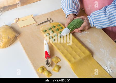 Traditionelle italienische Pasta. Präparationsphase von Ravioli mit Spinat und Ricotta mit einem Gebäckbeutel. Gekochter und gehackter Spinat auf hausgemachter Pasta Stockfoto