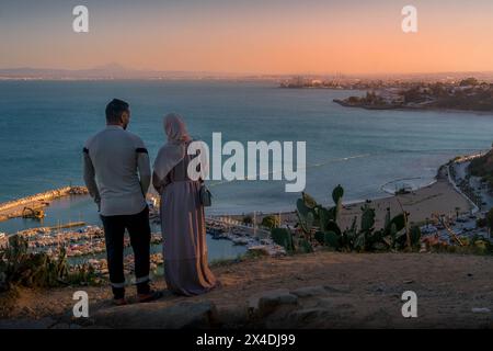 Das Paar, das an der Klippe von Sidi Bou Said stand, beobachtete das Mittelmeer, das Panorama der Stadt Tunis und den malerischen Sonnenuntergang. Stockfoto