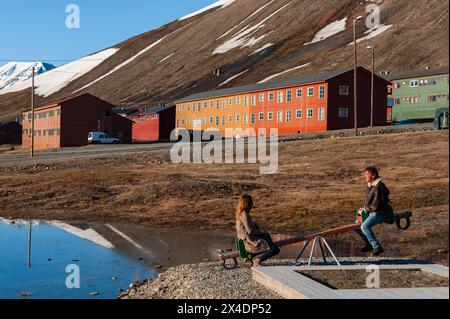 Erwachsene fahren mit einer Säge in der Nähe von hell bemalten Gebäuden in der Stadt Longyearbyen, Spitzbergen Island, Svalbard, Norwegen. (Nur Für Redaktionelle Zwecke) Stockfoto