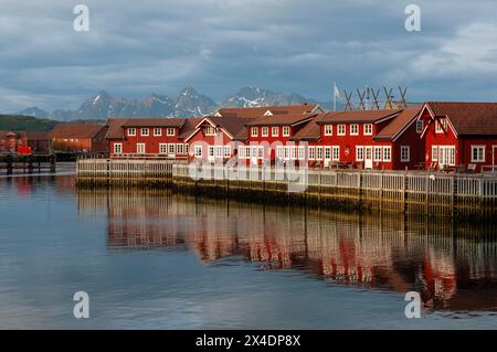 Hell bemalte, sonnendurchflutete Gebäude im Fischerdorf Svolvaer reflektieren das Hafenwasser. Austvagoya Island, Lofoten, Norwegen. Stockfoto