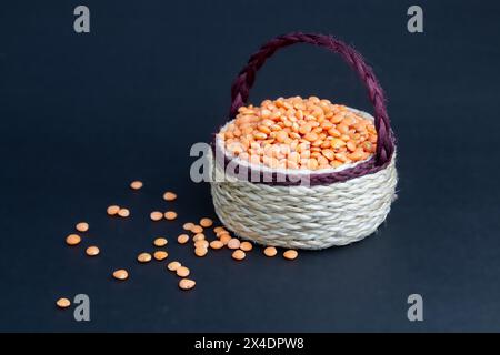 Rote Linsen stapeln sich isoliert. Trockene orangene Linsenkörner, Haufen von Dal, roh Daal, Dhal, Masoor, Lens culinaris oder Lens esculenta auf Jutekorb. Stockfoto