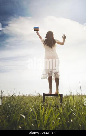 Surrealer Moment einer Frau auf einem Hocker, die mit ihrem Pinsel den Himmel malte, abstraktes Konzept Stockfoto