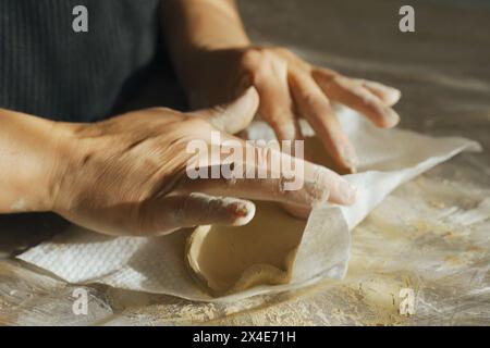 Eine Frau formt eine graue Tonplatte mit ihren Händen, Nahaufnahme. Basteln aus Lehm. Hobbys und Kreativität. Blick von oben Stockfoto