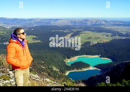 Ein Tourist genießt die Aussicht, während er auf einem Berg mit einem See im Hintergrund steht. Porträt eines Mannes im Profil während einer Wanderung in Durmitor Stockfoto