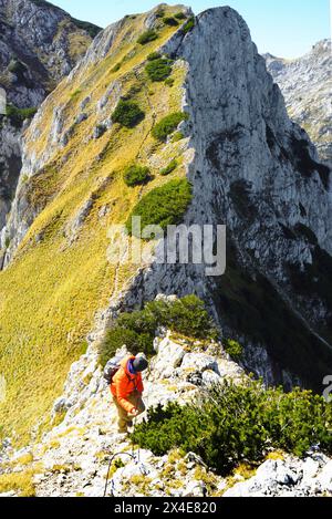 Vor dem Hintergrund einer wunderschönen Landschaft spaziert ein Wanderer durch eine gefährliche Bergregion, hält sich an einem Sicherheitsseil fest und blickt nach unten Stockfoto