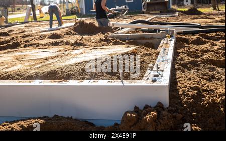 Neue Wohnbaustelle mit Betonblockmauerfundament und zwei Arbeitern auf dem Boden, wo die Platte in Kürze verlegt werden soll. Stockfoto