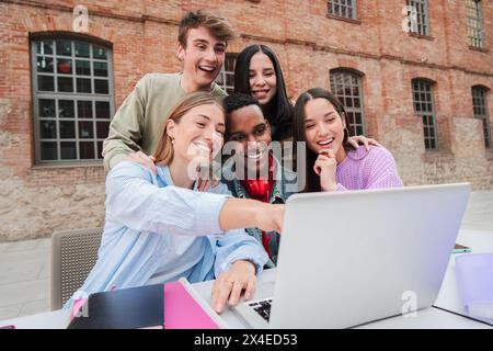 Eine Gruppe multirassischer Teenager-Schüler lächelt mit einem Laptop, um Informationen für die Hausarbeiten der Highschool zu suchen. Klassenkameraden, die für eine Prüfung studieren Stockfoto