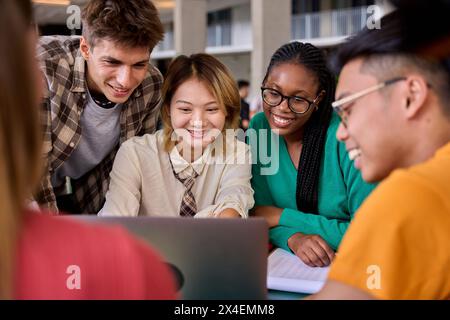 Gruppe von verschiedenen multiethnischen, lächelnden jungen Studenten, die mit einem Laptop lernen und sich im Klassenzimmer treffen Stockfoto