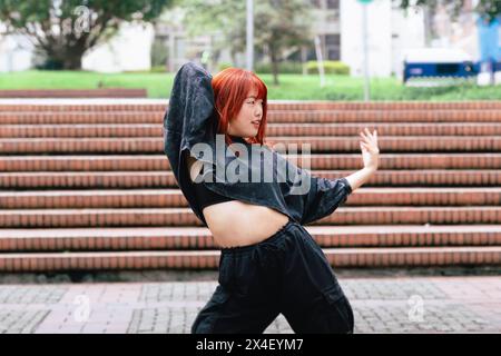 Junge Koreanerin in lässiger Kleidung tanzt mit Begeisterung auf der Stadtreppe Stockfoto