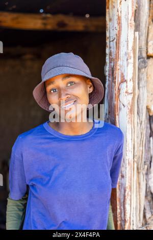 afrikanisches Dorf, alleinerziehendes Teenager-Mädchen vor der Tür draußen, Schlammhütten innen schmutzige Wände Stockfoto