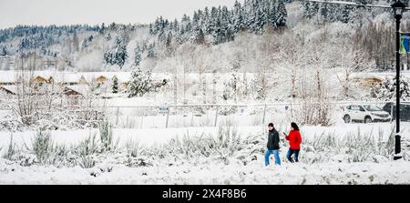 USA, Washington State, Woodinville. Ein Mann und eine Frau im roten Mantel spazieren im Schnee in Woodinville. (Nur Für Redaktionelle Zwecke) Stockfoto