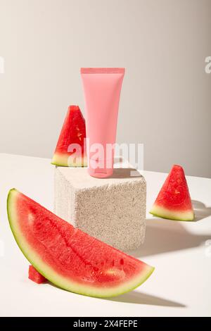 Auf weißem Hintergrund, eine rosafarbene Kunststoffröhre auf dem Steinpodium mit frischen saftigen Wassermelonenscheiben. Vorderansicht, Mockup-Szene für Werbekosmos Stockfoto