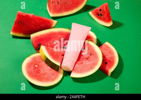 Mockup-Szene für Werbung für Kosmetik. Kosmetikflasche und Wassermelonenscheiben auf grünem Hintergrund. Wassermelone ist mit Vitamin C gefüllt, das sofort Stockfoto