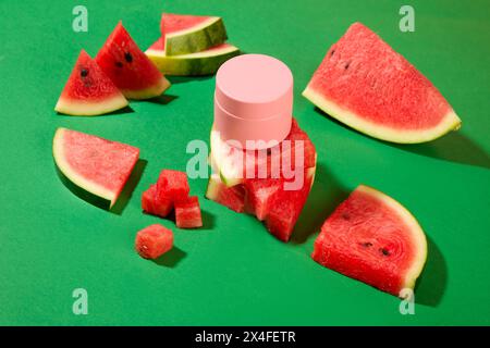 Vor dem grünen Hintergrund, frische Wassermelonenscheiben mit Kosmetikglas dekoriert. Mockup-Szene für Design. Wassermelone ist reich an Vitamin C und Antiox Stockfoto