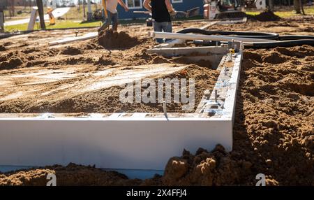 Neue Wohnbaustelle mit Betonblockmauerfundament und zwei Arbeitern auf dem Boden, wo die Platte in Kürze verlegt werden soll. Stockfoto