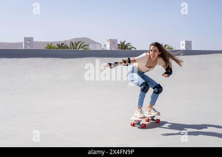 Eine junge Frau, eine Anfängerin im Surfskating-Sport, fährt selbstbewusst auf ihrem Skateboard die Seite einer Rampe hinunter. Stockfoto