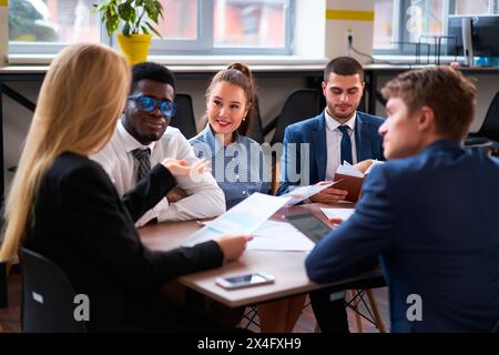 Multiethnische Geschäftsteams beteiligen sich an einer gemeinsamen Besprechung in modernen Büros. Afrikanische, asiatische und kaukasische Kollegen analysieren Daten, diskutieren Strategien Stockfoto