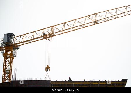 Ein gelber Baukran auf der Höhe eines Gebäudes hebt eine Last mit einem Haken an. Mitarbeiter am Rande. Stockfoto