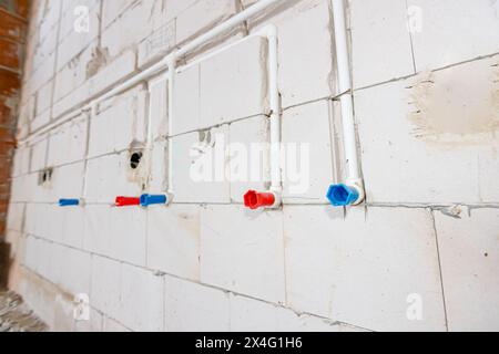 Neue unfertige Installationen freiliegender weißer PVC-Rohre, die in der Wand montiert sind. Rote und blaue Röhrchen sind für heißes und kaltes Wasser geeignet. Stockfoto