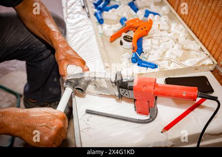 Klempnerhände wie mit handlichem Elektrowerkzeug, Lötkolben, Schweißen von Polypropylenrohren, Verbindung in Rohrleitungen, Werkstatt im Innenbereich Stockfoto