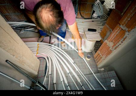 Arbeiter montieren neue Verteilerventile aus Messing für Zentralheizungsböden in einem im Bau befindlichen Wohngebäude. Stockfoto