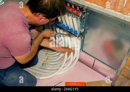 Arbeiter montieren neue Verteilerventile aus Messing für Zentralheizungsböden in einem im Bau befindlichen Wohngebäude. Stockfoto