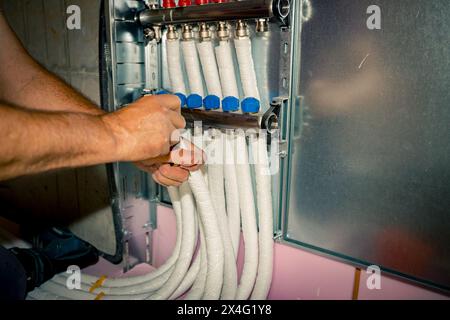 Arbeiter montieren neue Verteilerventile aus Messing für Zentralheizungsböden in einem im Bau befindlichen Wohngebäude. Stockfoto