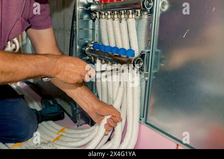 Arbeiter montieren neue Verteilerventile aus Messing für Zentralheizungsböden in einem im Bau befindlichen Wohngebäude. Stockfoto