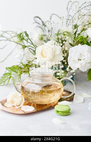 Ästhetische Tischeinstellung. Grüne Teekanne, Makronen-Desserts, weiße Rosen und Eustomas. Zeit für dich, Ruhe, Kern, langsam leben Konzept Stockfoto