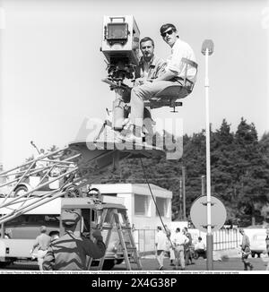 Dreharbeiten im Jahr 1963. Ein Kameramann und sein Assistent sitzen auf einer beweglichen Plattform während der Dreharbeiten eines Werbespots für die Benzinfirma Esso. Mit einer Linse vor einem Auge nimmt der Kameramann eine Messung des Lichts vor. Kristoffersson Ref. DC98-6 Stockfoto