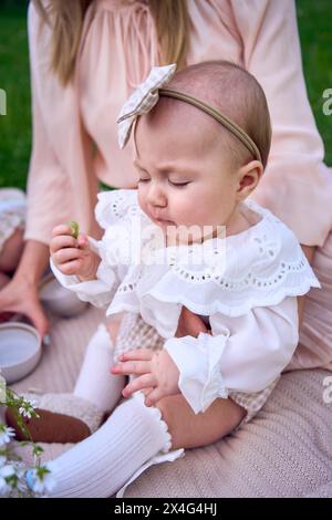 Das kleine Mädchen isst Trauben in den Armen ihrer Mutter Stockfoto