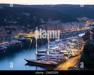 Bonifacio, Corse-du-Sud, Korsika, Frankreich. Blick über den beleuchteten Hafen in der Abenddämmerung, Luxusyachten, die am Kai vertäut sind. Stockfoto