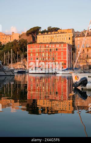 Bastia, Haute-Corse, Korsika, Frankreich. Blick über den Vieux Port bei Sonnenaufgang, farbenfrohe Hafenhäuser, die sich im ruhigen Wasser spiegeln. Stockfoto