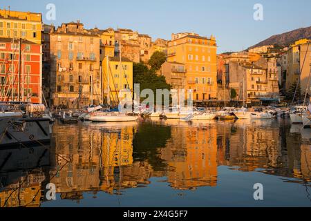 Bastia, Haute-Corse, Korsika, Frankreich. Blick über den Vieux Port bei Sonnenaufgang, farbenfrohe Hafenhäuser, die sich im ruhigen Wasser spiegeln. Stockfoto