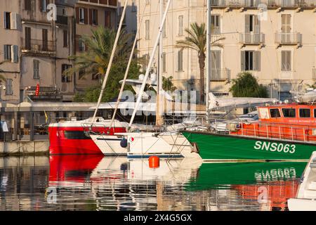 Bonifacio, Corse-du-Sud, Korsika, Frankreich. Blick über den Hafen bei Sonnenaufgang, farbenfrohe, verankerte Boote spiegeln sich im ruhigen Wasser. Stockfoto