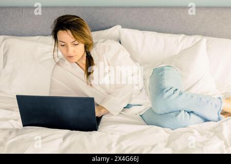 Frau mit Laptop, die zu Hause im Bett arbeitet Stockfoto
