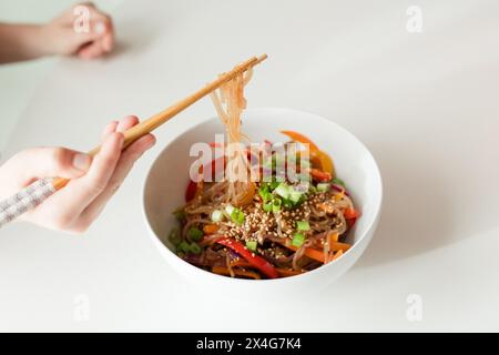 Genießen Sie eine Schüssel mit bunten Gemüsenudeln mit Essstäbchen Stockfoto