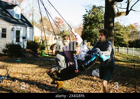 Teenager schiebt jüngere Cousins auf Baumschaukel im Vorgarten Stockfoto