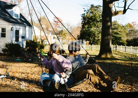 Cousins auf Bäumen schwingen im Vorgarten unter Bäumen im Herbst Stockfoto