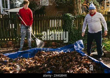 Opa und Teenager halten im Herbst Blätter auf Plane auf dem Hof Stockfoto