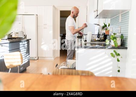 Mann, der in einer sonnigen und hellen Küche Geschirr tut Stockfoto