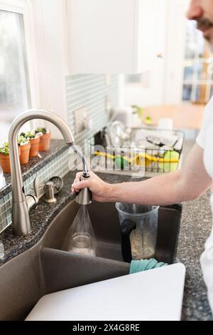 Mann, der schmutziges Geschirr in einer weißen Küche sprüht Stockfoto