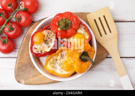 Köstliche gefüllte Paprika in der Schüssel, frische Tomaten und Spatel auf weißem Holztisch, flach gelegt Stockfoto