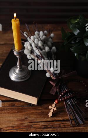 Rosenkranzperlen, Bibel, brennende Kerze und Weidenzweige auf Holztisch Stockfoto