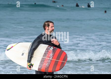 Ein müder Surfer mit seinem unverwechselbaren Surfbrett nach einer Surfsession in Fistral in Newquay in Cornwall in Großbritannien. Stockfoto