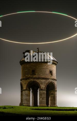 Geheimnisvoller mittelalterlicher Turm, beleuchtet von einem runden Lichtpfad vor einem nebeligen Nachthimmel Stockfoto