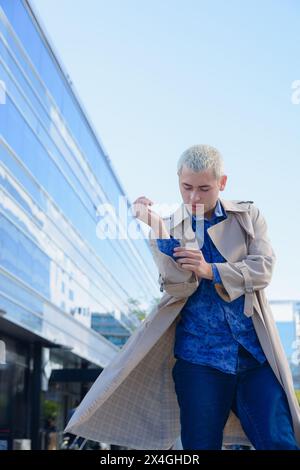 Vertikales Bild für soziale Netzwerke eines jungen Mannes, der außerhalb von Arbeitsgebäuden steht und seine Jacke fixiert Stockfoto