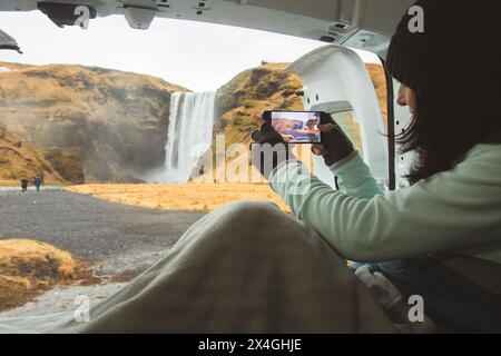 Reisender Frau fotografieren Sie Videofoto des wunderschönen Wasserfalls Verwenden Sie Smartphone. Weibliche Touristen fotografieren mit der Handykamera während der Reise auf Isländisch Stockfoto