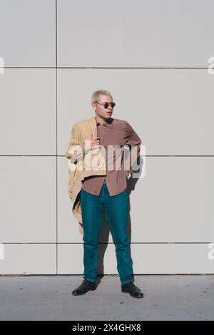 Vertikales Bild eines jungen Mannes, der bereit ist, zu gehen, er steht und seine Jacke anzieht, er trägt eine Sonnenbrille. Stockfoto