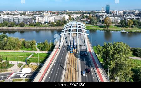 Krakau, Polen. Zwei blaue Straßenbahnen, die sich auf der Kotlarski-Hängebrücke mit vierspuriger Straße, Straßenbahnlinie, Fußgängerbrücke und rotem Fahrradweg über VI überqueren Stockfoto